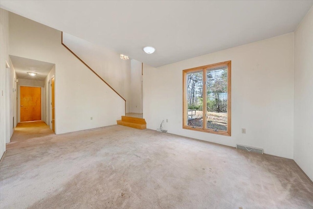 unfurnished living room featuring stairway, visible vents, and light colored carpet
