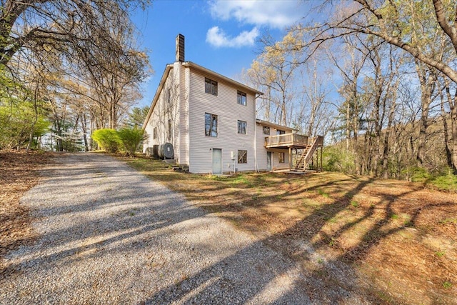 view of side of home featuring a chimney, stairway, a deck, and gravel driveway
