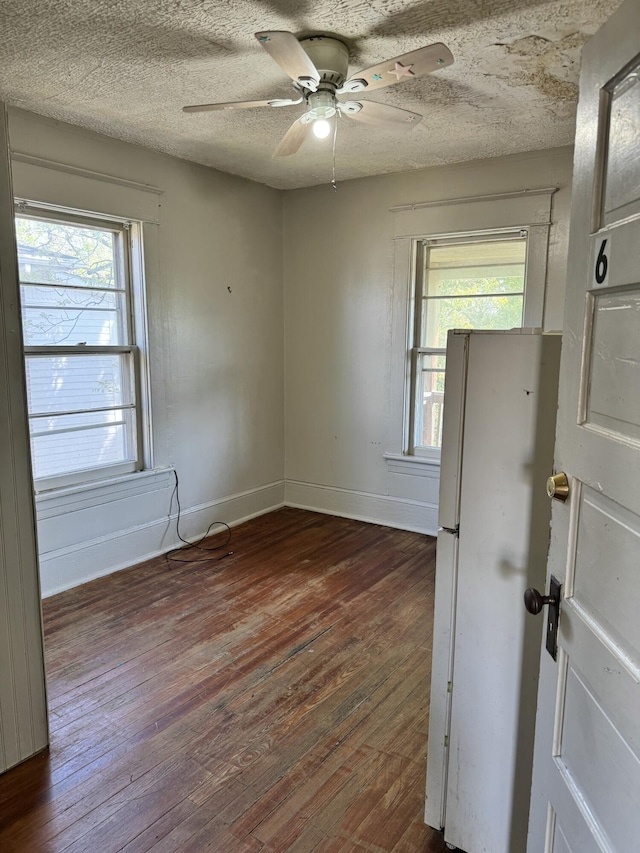spare room featuring wood-type flooring, a ceiling fan, baseboards, and a wealth of natural light