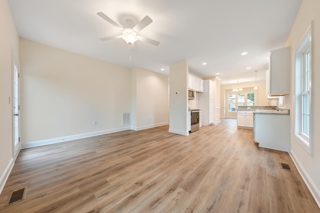 unfurnished living room with a ceiling fan, light wood-style floors, visible vents, and a sink
