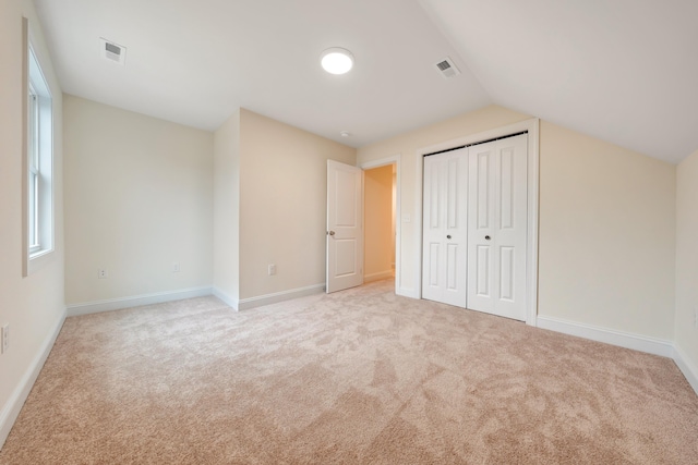unfurnished bedroom with visible vents, baseboards, lofted ceiling, and light carpet