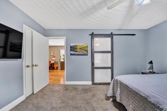 bedroom featuring ceiling fan, a textured ceiling, carpet floors, a barn door, and baseboards