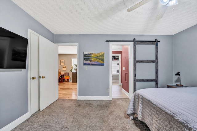 bedroom with baseboards, a textured ceiling, carpet floors, a barn door, and ceiling fan
