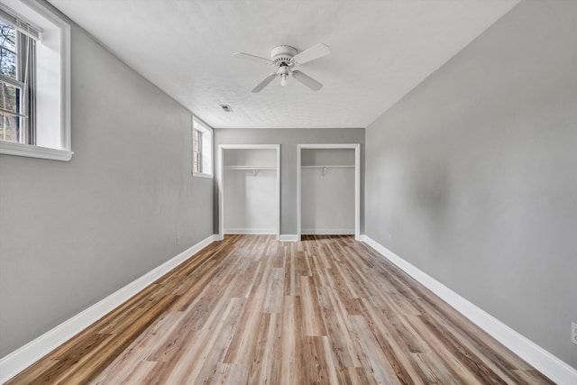 unfurnished bedroom featuring light wood-style flooring, a ceiling fan, visible vents, multiple closets, and baseboards