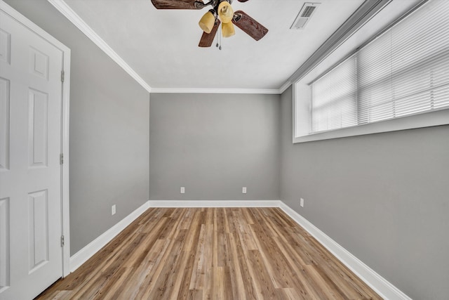 spare room featuring baseboards, light wood-type flooring, ornamental molding, a ceiling fan, and visible vents