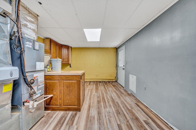 kitchen with light countertops, brown cabinetry, a drop ceiling, and light wood-style floors