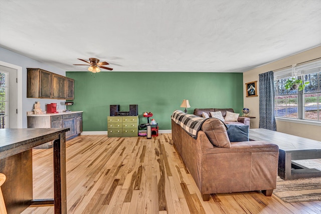 living area with light wood-style flooring, a ceiling fan, and baseboards