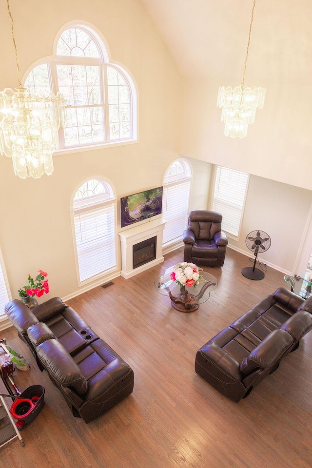 living room with wood finished floors, a fireplace, visible vents, baseboards, and a chandelier