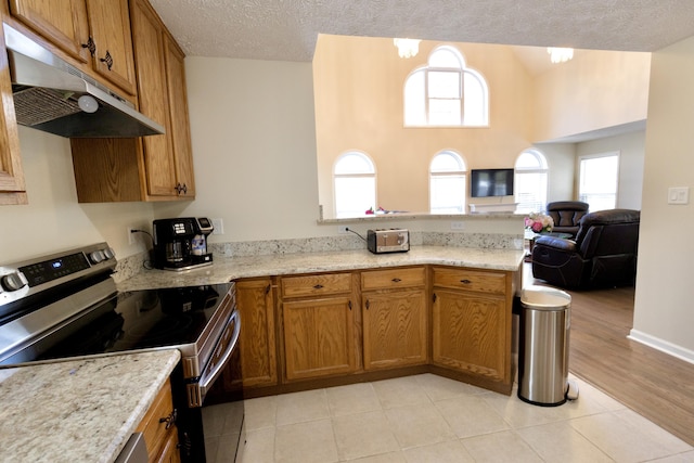 kitchen with stainless steel electric stove, brown cabinetry, under cabinet range hood, and a peninsula