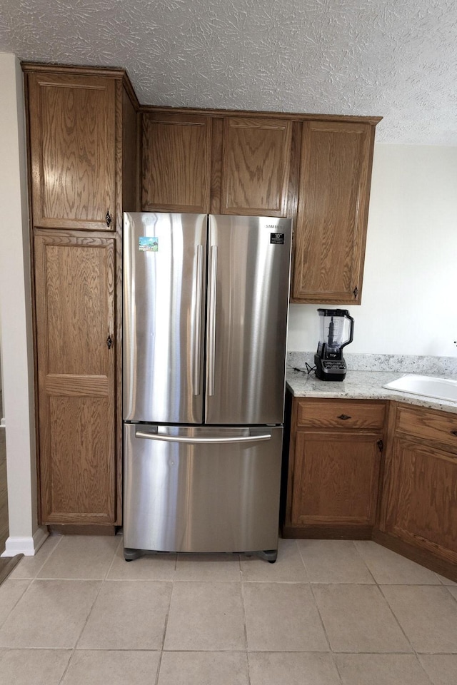 kitchen featuring brown cabinets, light tile patterned floors, a sink, freestanding refrigerator, and a textured ceiling