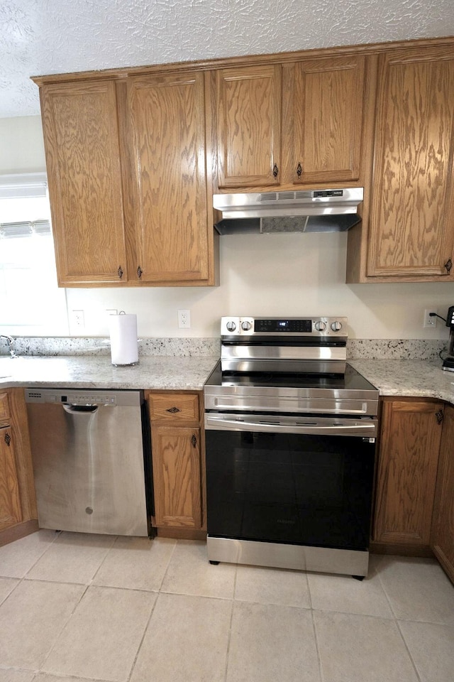 kitchen with stainless steel appliances, under cabinet range hood, a textured ceiling, and light tile patterned floors
