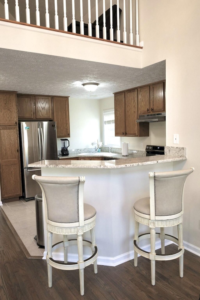 kitchen featuring light wood-type flooring, a peninsula, under cabinet range hood, and appliances with stainless steel finishes