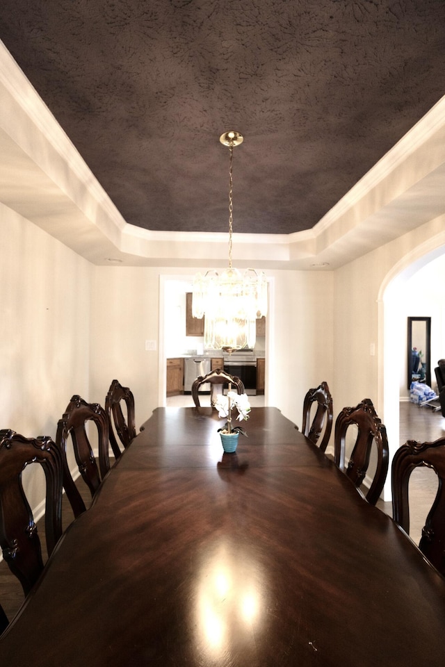 dining space featuring a tray ceiling, arched walkways, and an inviting chandelier