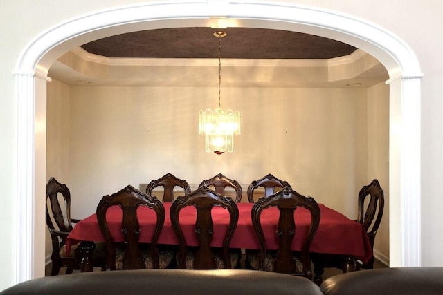 dining space featuring arched walkways, a tray ceiling, ornamental molding, and an inviting chandelier