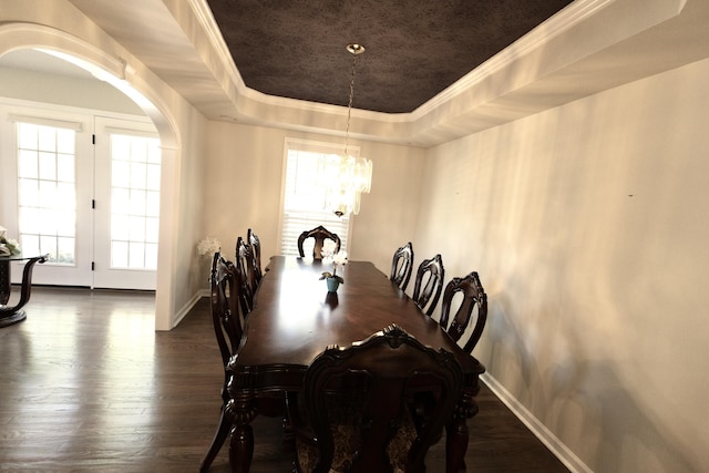 dining room featuring baseboards, arched walkways, dark wood-style flooring, and a raised ceiling