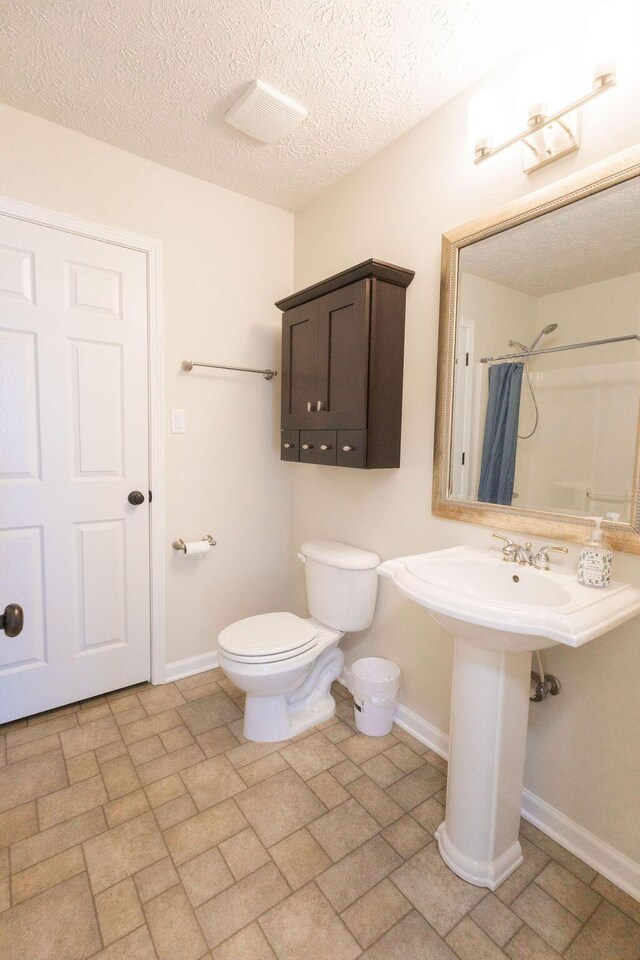 bathroom with baseboards, toilet, a shower with shower curtain, and a textured ceiling