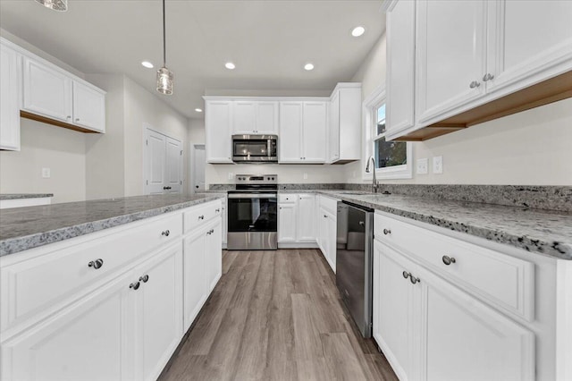 kitchen with appliances with stainless steel finishes, light stone countertops, a sink, light wood-style floors, and white cabinetry