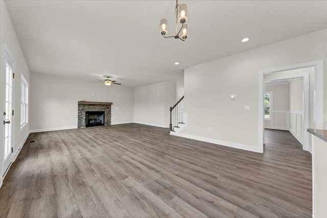 unfurnished living room featuring a fireplace, ceiling fan with notable chandelier, stairs, and wood finished floors