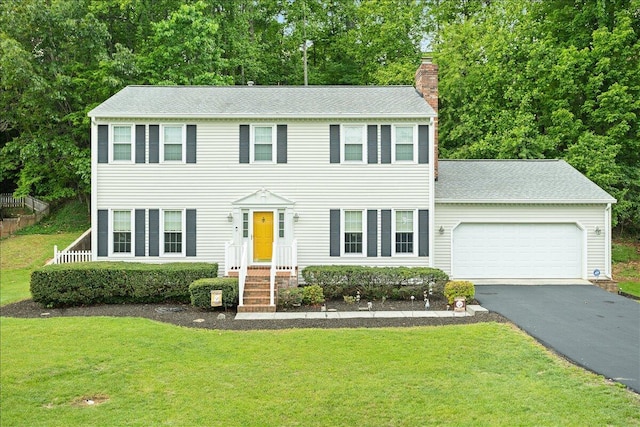 colonial inspired home with a chimney, asphalt driveway, a garage, a front yard, and roof with shingles