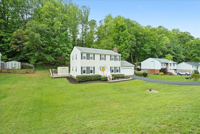 colonial-style house with an outdoor structure, a chimney, a front yard, and a detached garage