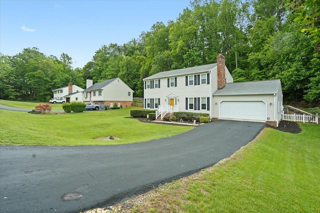 colonial inspired home featuring asphalt driveway, an attached garage, a chimney, and a front yard