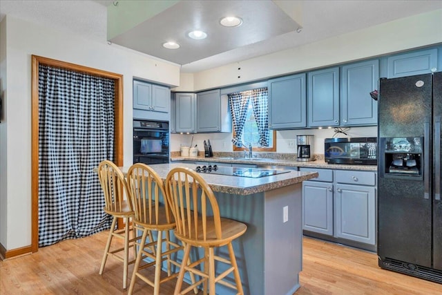 kitchen featuring black appliances, light wood-style flooring, a center island, and a kitchen bar