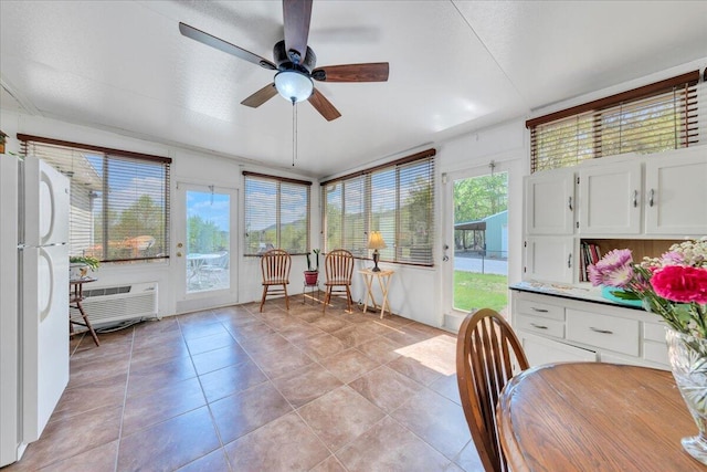 sunroom with a wall unit AC, a ceiling fan, and tile patterned floors
