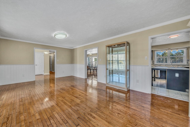 unfurnished living room featuring hardwood / wood-style floors, wainscoting, a textured ceiling, and crown molding