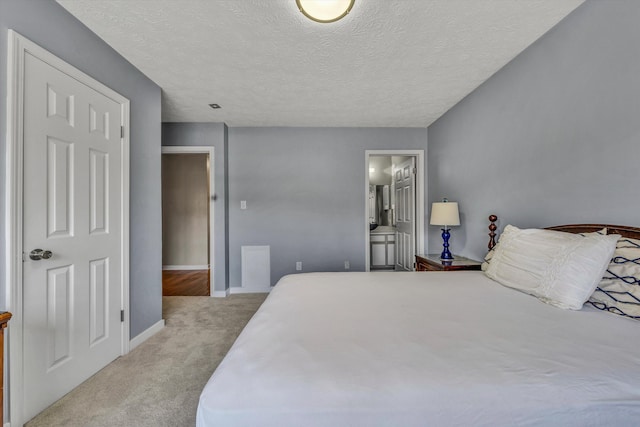 carpeted bedroom featuring a textured ceiling, baseboards, and ensuite bathroom