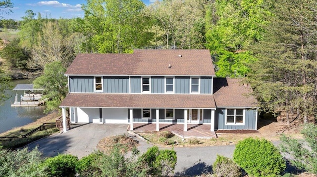 back of property featuring a water view, board and batten siding, driveway, a porch, and roof with shingles