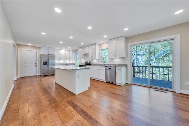 kitchen with a center island, stainless steel appliances, light wood finished floors, white cabinets, and visible vents