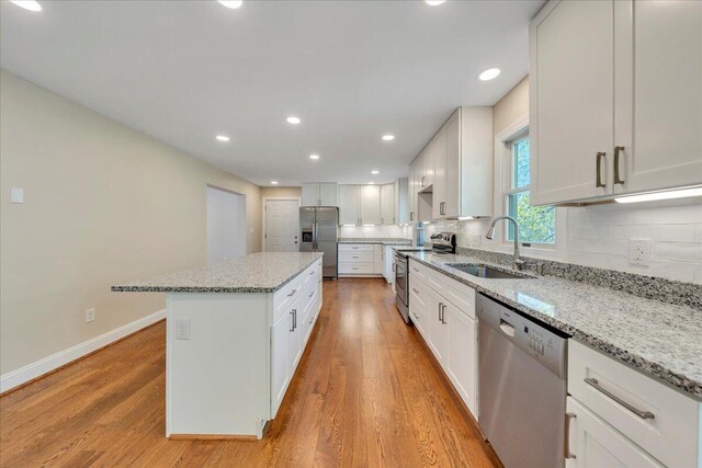 kitchen with stainless steel appliances, a sink, light wood-type flooring, light stone counters, and a kitchen island