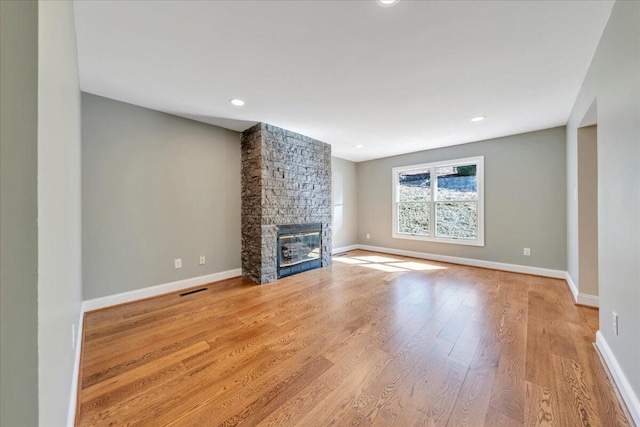 unfurnished living room with a fireplace, wood finished floors, visible vents, and baseboards