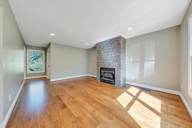 unfurnished living room with wood finished floors, a stone fireplace, baseboards, visible vents, and recessed lighting