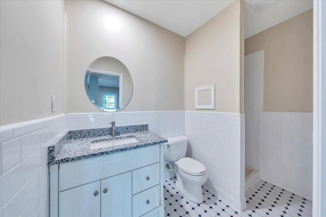 bathroom with tile walls, a wainscoted wall, vanity, and toilet