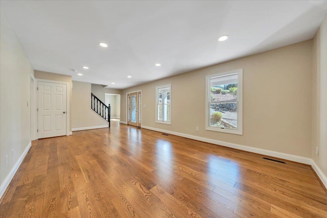 unfurnished living room with baseboards, wood finished floors, stairs, and visible vents
