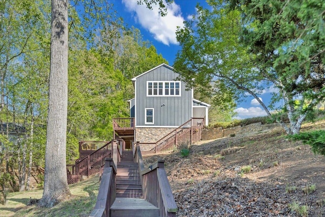 exterior space with board and batten siding, a wooden deck, stone siding, and stairs