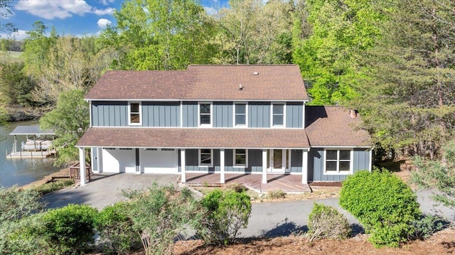 back of house with driveway, a water view, board and batten siding, covered porch, and an attached garage