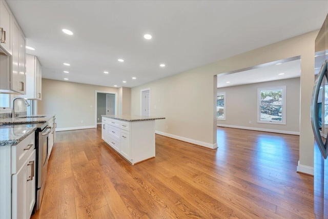 kitchen featuring a sink, stainless steel electric stove, light wood finished floors, white cabinetry, and a kitchen island
