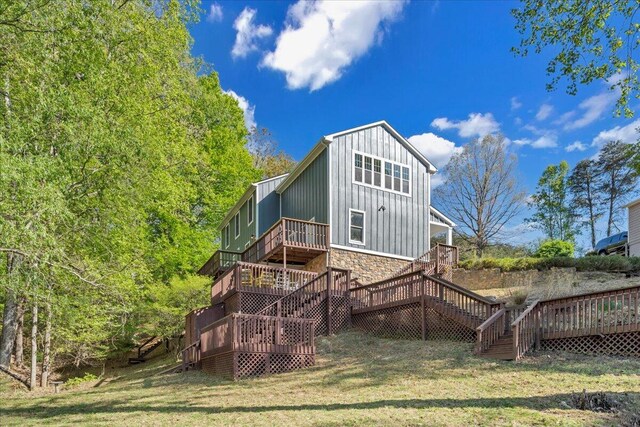 rear view of house with stone siding, a wooden deck, stairs, board and batten siding, and a yard