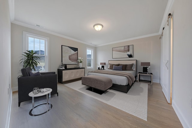 bedroom featuring a barn door, visible vents, crown molding, light wood-style flooring, and baseboards
