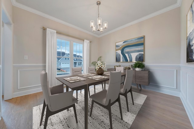 dining room with a decorative wall, wood finished floors, a chandelier, crown molding, and wainscoting