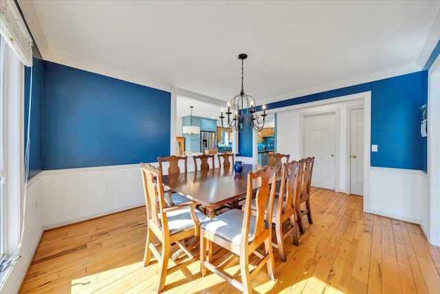 dining room with wainscoting, light wood-style flooring, a chandelier, and crown molding