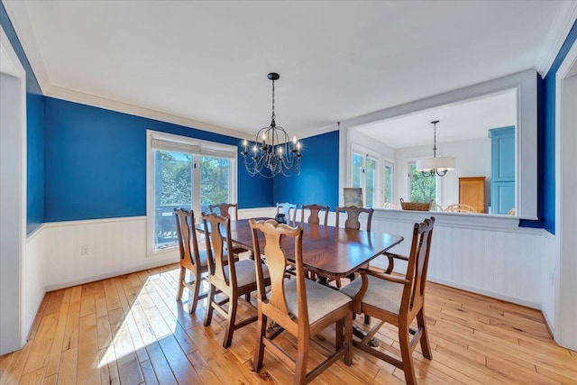 dining room featuring light wood finished floors, ornamental molding, a wainscoted wall, and a notable chandelier