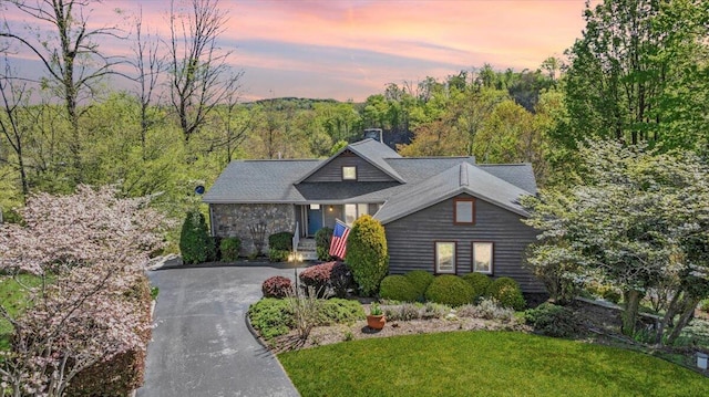 view of front of house with a view of trees, aphalt driveway, and a front yard