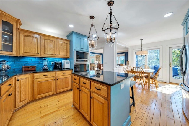 kitchen featuring stainless steel appliances, a chandelier, light wood-style floors, glass insert cabinets, and hanging light fixtures