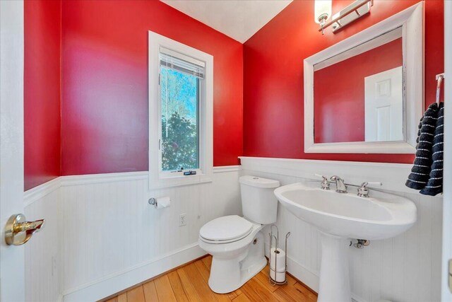 half bathroom with wood finished floors, toilet, a sink, and wainscoting