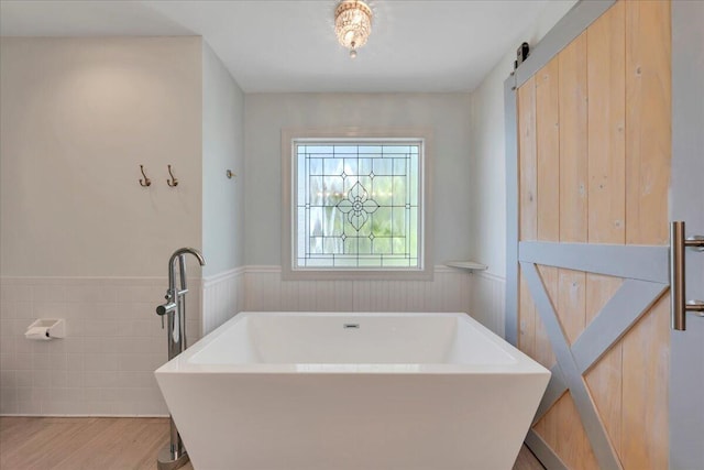 bathroom with a freestanding tub, a wainscoted wall, and wood finished floors