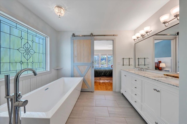 full bathroom featuring a wainscoted wall, a freestanding bath, double vanity, a sink, and connected bathroom