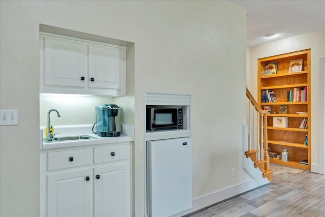 bar featuring stairway, built in fridge, a sink, black microwave, and light wood-style floors